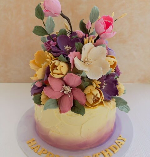 ribbon cake covered in butter icing and decorated with hand made sugar flowers