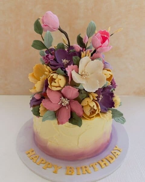 ribbon cake covered in butter icing and decorated with hand made sugar flowers
